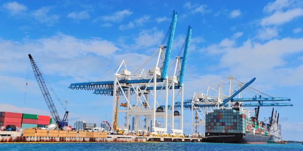 Cargo ship at Miami harbor with crane and blue sky over sea.